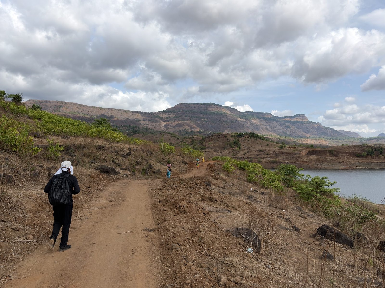 Trail leading down toward Dhom Dam with a hiker in the foreground